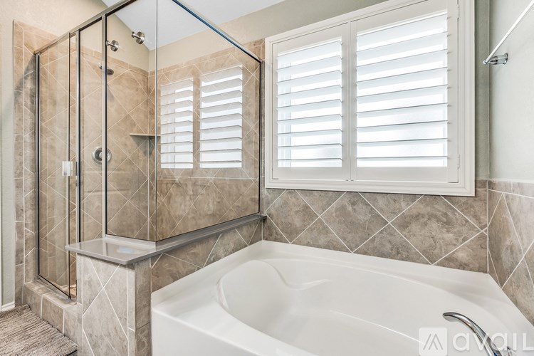 A white bathtub sits under a window with white blinds in a bathroom.