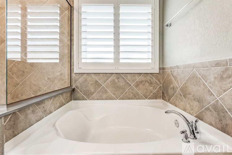 A white bathroom sink with a white tub and white shutters on the window.