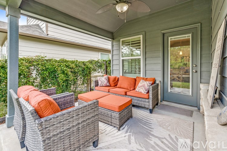 A patio with a grey wicker sofa and orange cushions.
