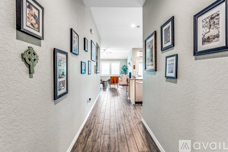 A hallway with a white wall and a wooden floor with pictures on the wall.