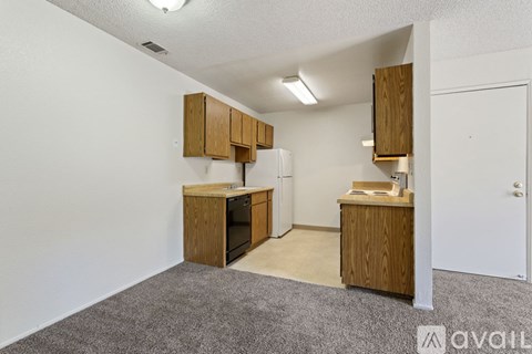 A kitchen area with wooden cabinets and appliances in a room with carpeted flooring.