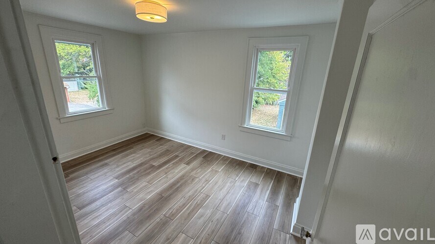 A room with wooden flooring and two windows.