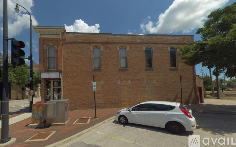 A white car is parked on the side of a street in front of a brick building.