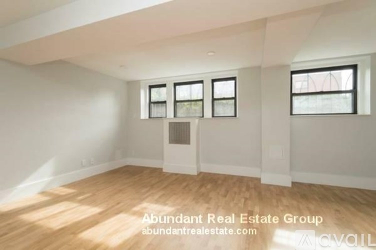 A spacious room with wooden flooring and white walls, featuring a large window with a view of a construction site outside.