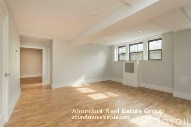 A spacious room with wooden flooring and white walls, with a door on the left and a window with blinds on the right.