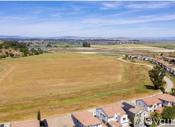 A large open field with a few houses and trees in the distance.
