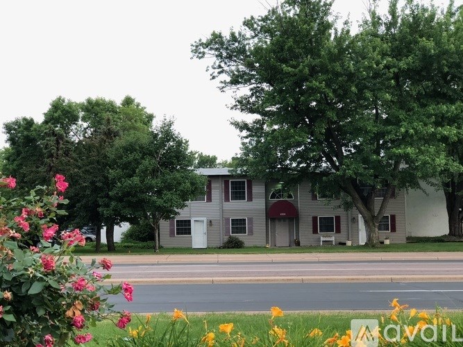 A grey house with a red awning is surrounded by trees and flowers.