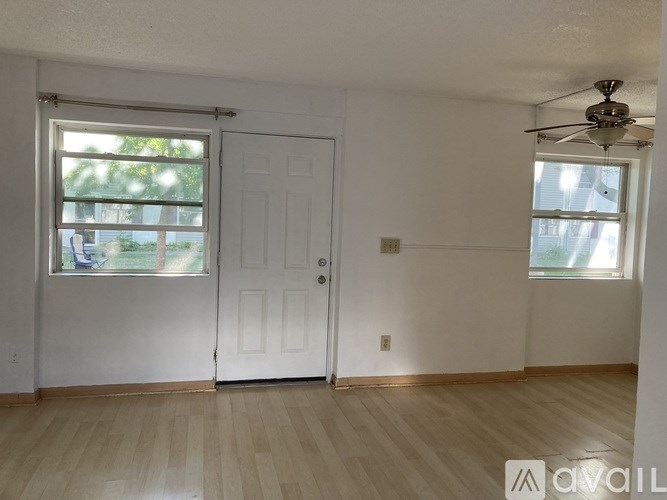 A room with a white door and a window with a fan on the ceiling.