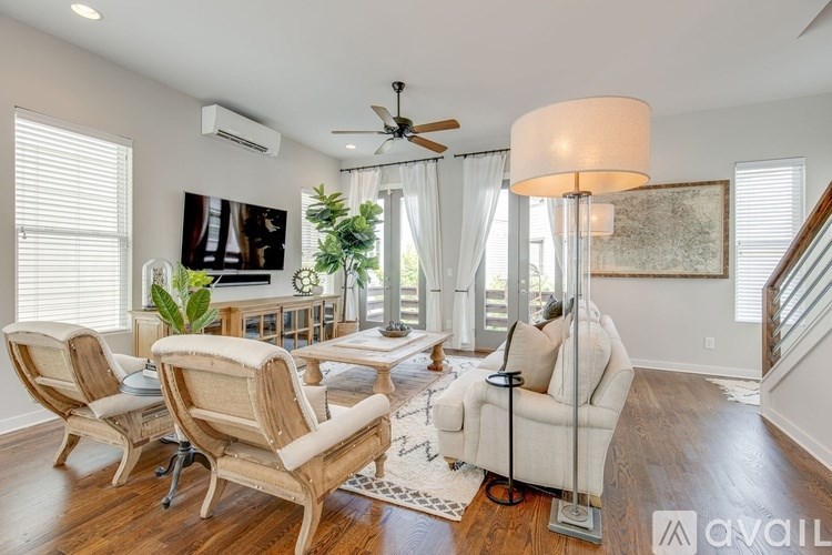 A living room with a white couch, a chair, a table, a plant, a painting, a ceiling fan, and a rug.
