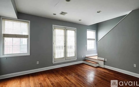 A room with wooden floors and grey walls has two windows and a staircase.