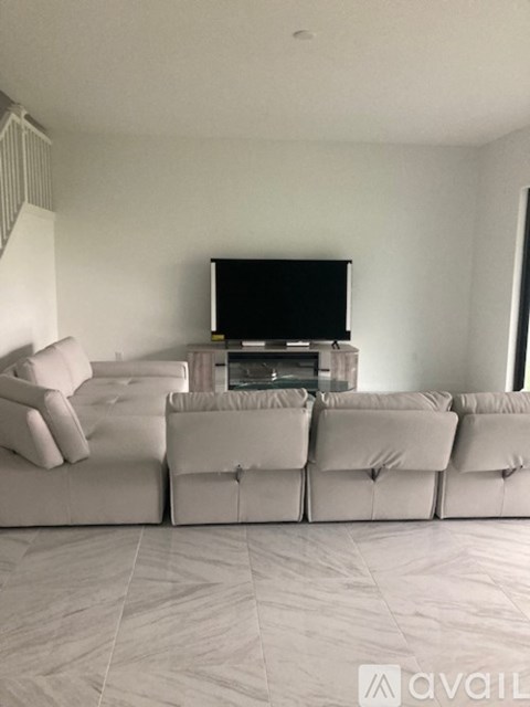 A living room with a television and a row of white couches.