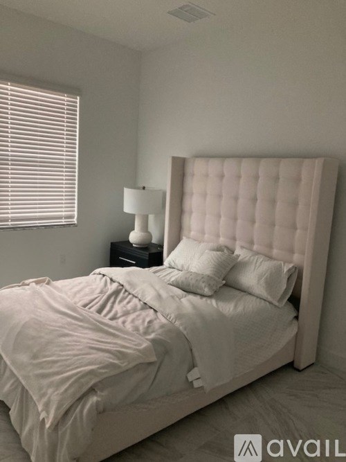 A bed with a white headboard and pillows is in a room with a lamp on a side table.