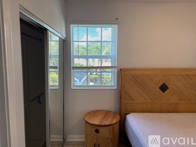 A bedroom with a bed, wooden stool, and a window with blinds.