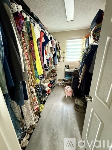 A person is standing in a hallway with a white door on the right and a closet full of clothes on the left.