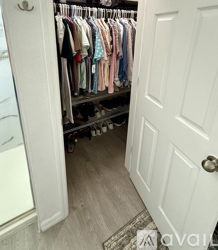 A white closet with clothes hanging on shelves and a white door.