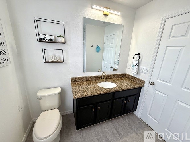 A bathroom with a toilet, sink, mirror, and cabinets.