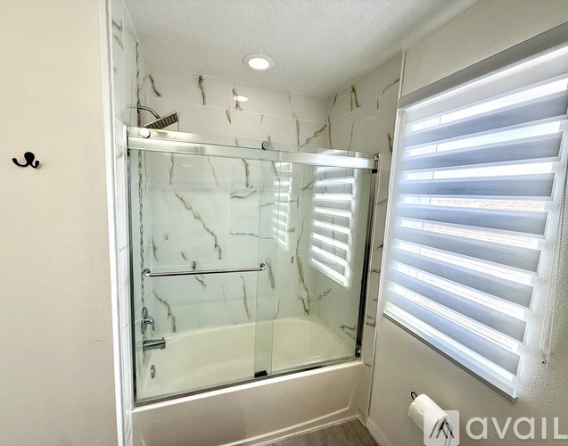 A bathroom with a glass shower door and a window with blinds.