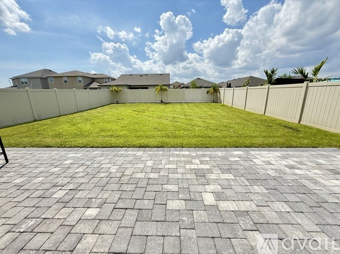 A backyard with a brick patio and a white fence.