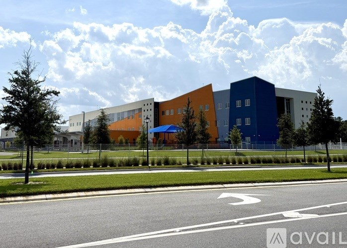 A modern building with a blue and orange facade is surrounded by a grassy area and trees.