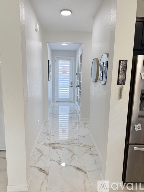 A hallway with marble flooring and a refrigerator on the right.