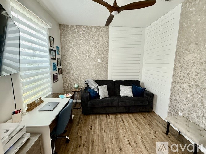 A room with a couch, a desk, and a ceiling fan.