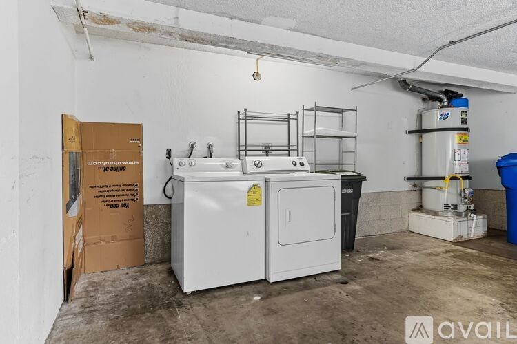A room with a white fridge, a cardboard box, a blue container and a yellow caution tape on the fridge.