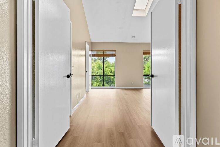 A hallway with a white door on the left and a balcony with a view of trees on the right.