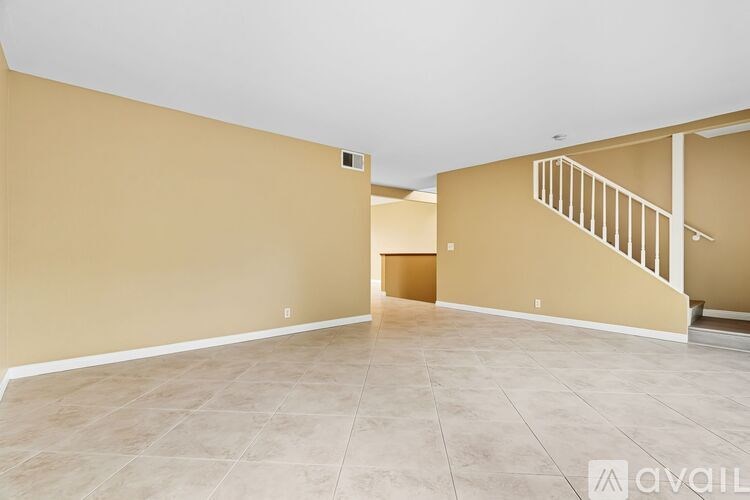 A spacious living room with beige walls and tiled flooring.
