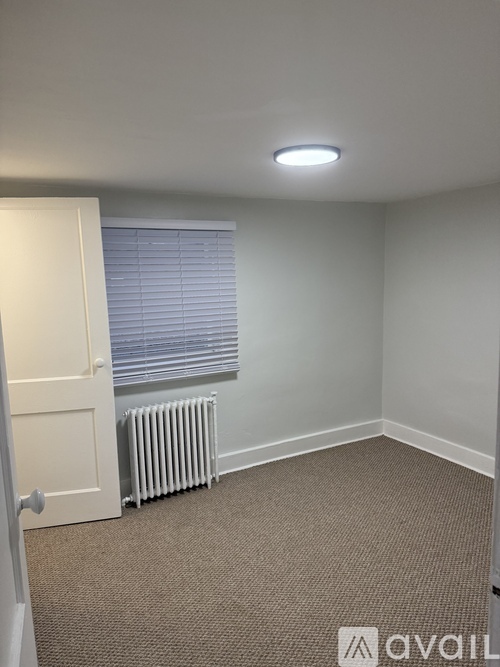 A carpeted room with a door, window, and a radiator.