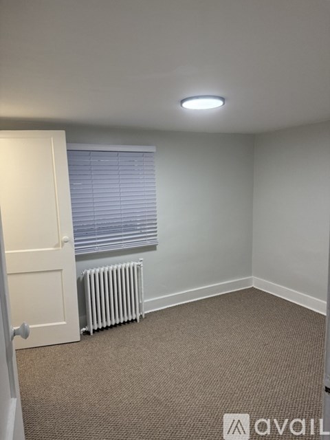 A carpeted room with a door, window, and a radiator.