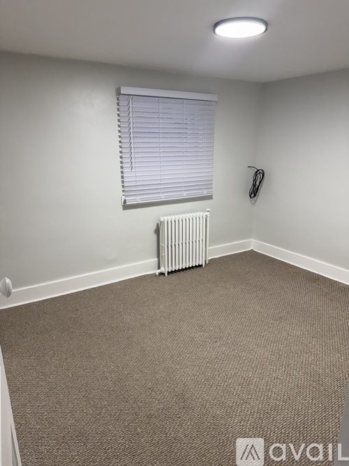 A carpeted room with a window and a radiator.
