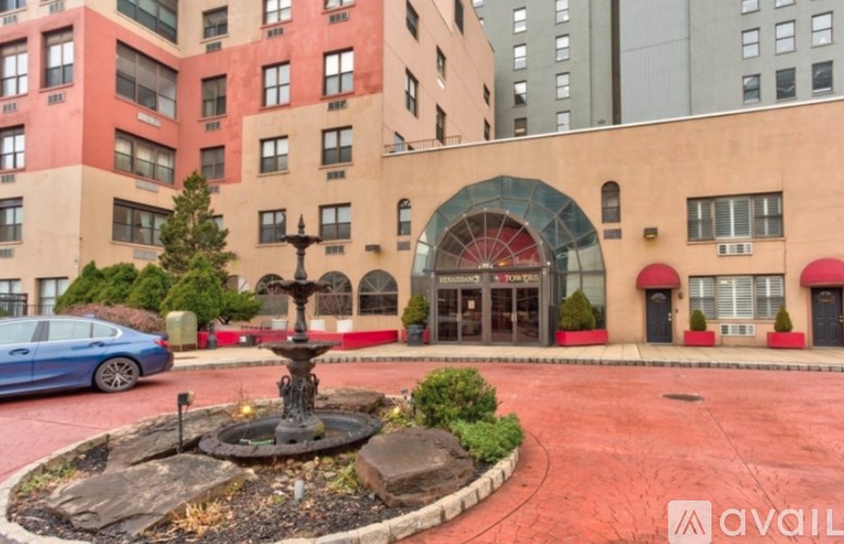 A blue car is parked in front of a building with a red brick courtyard and a fountain.