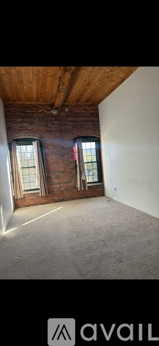 A room with a wooden ceiling and a window with a red curtain.