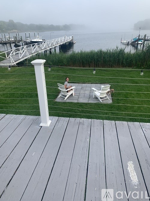 A woman is sitting on a white chair on a wooden deck overlooking a body of water.
