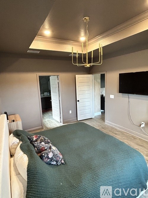 A bedroom with a bed covered in a green blanket and a chandelier hanging from the ceiling.