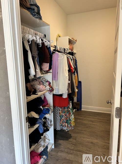 A white closet with clothes hanging on shelves and a door on the right.