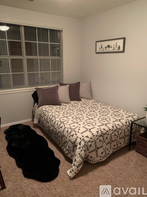 A bedroom with a bed, pillows, a black dog, and a framed picture on the wall.