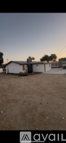 A house with a white exterior and a brown roof is surrounded by a dirt lot.