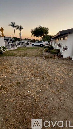 A dirt area with a white building and a car in the background.