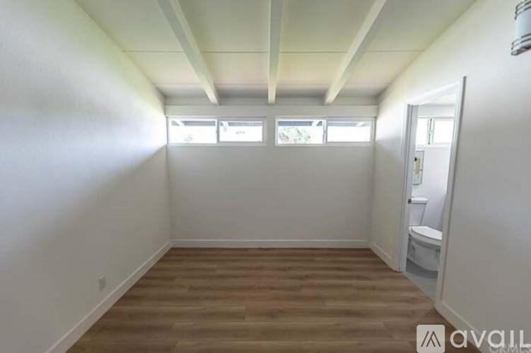 A room with wooden flooring and white walls, with a toilet visible in the corner.