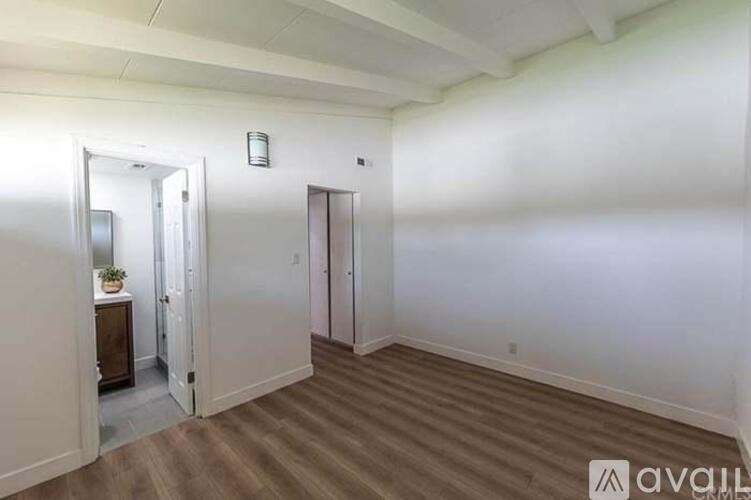 A room with a wooden floor and white walls, with a door and a mirror visible.