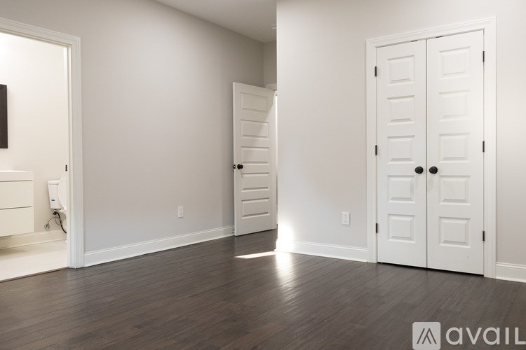 A room with white walls and a wooden floor with a white door and a white wardrobe.