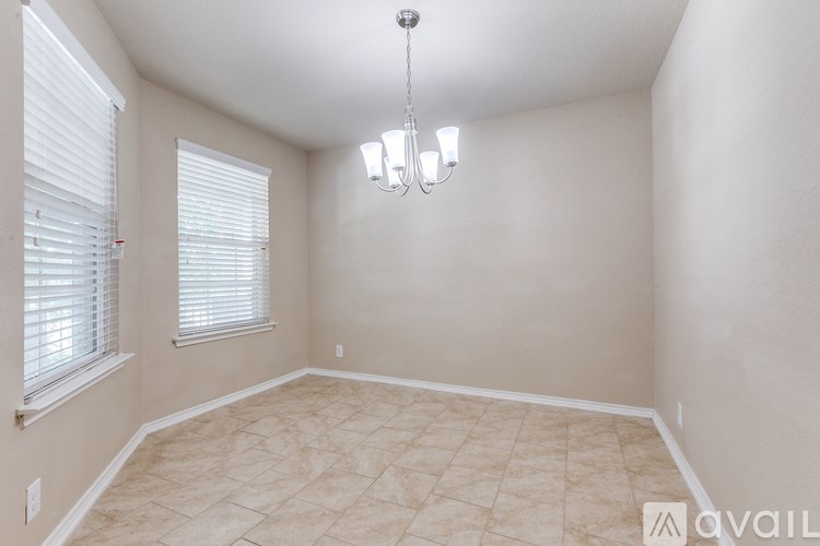 A room with a chandelier, tiled floor, and a window with blinds.