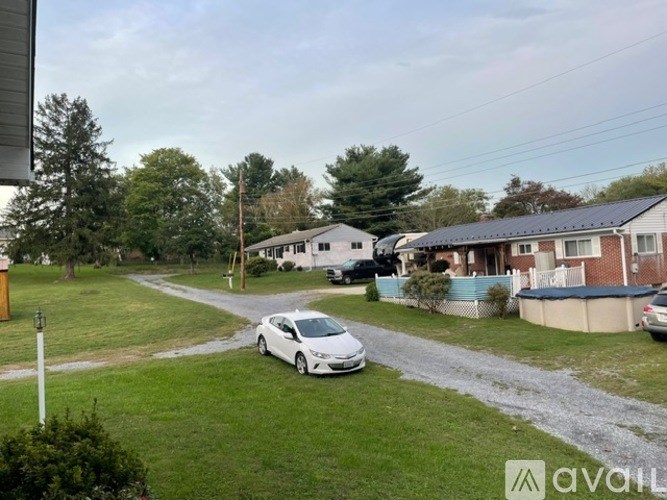 A white car is parked on a gravel driveway in front of a house.