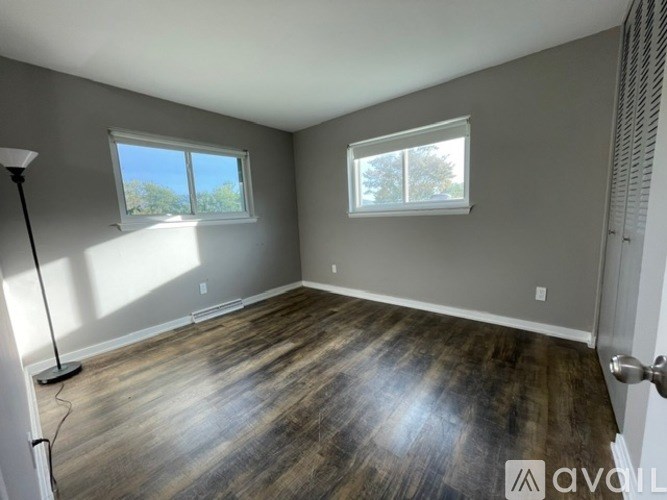 A room with wooden flooring and two windows.