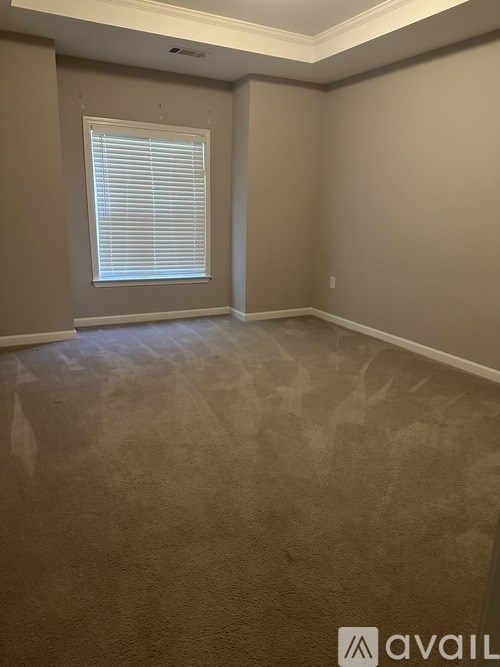 A room with beige walls and carpeting, a window with blinds, and a logo that reads "AVAIL".