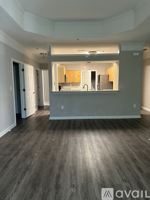 A spacious room with wooden flooring and a kitchen area in the background.