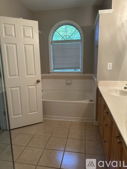A bathroom with a white door, a bathtub, a window with blinds, and a sink.