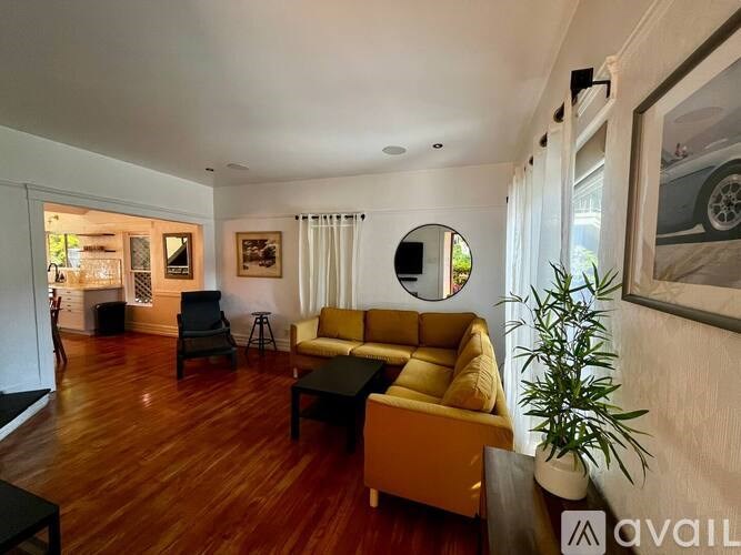 A living room with a yellow couch and a round mirror on the wall.