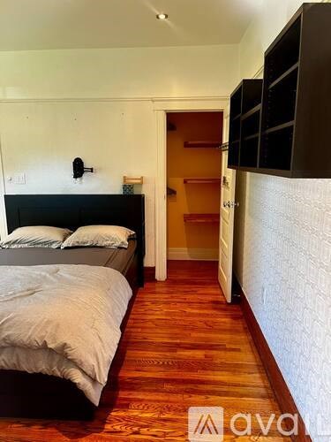 A bedroom with a bed, wooden floors, and a white wall.